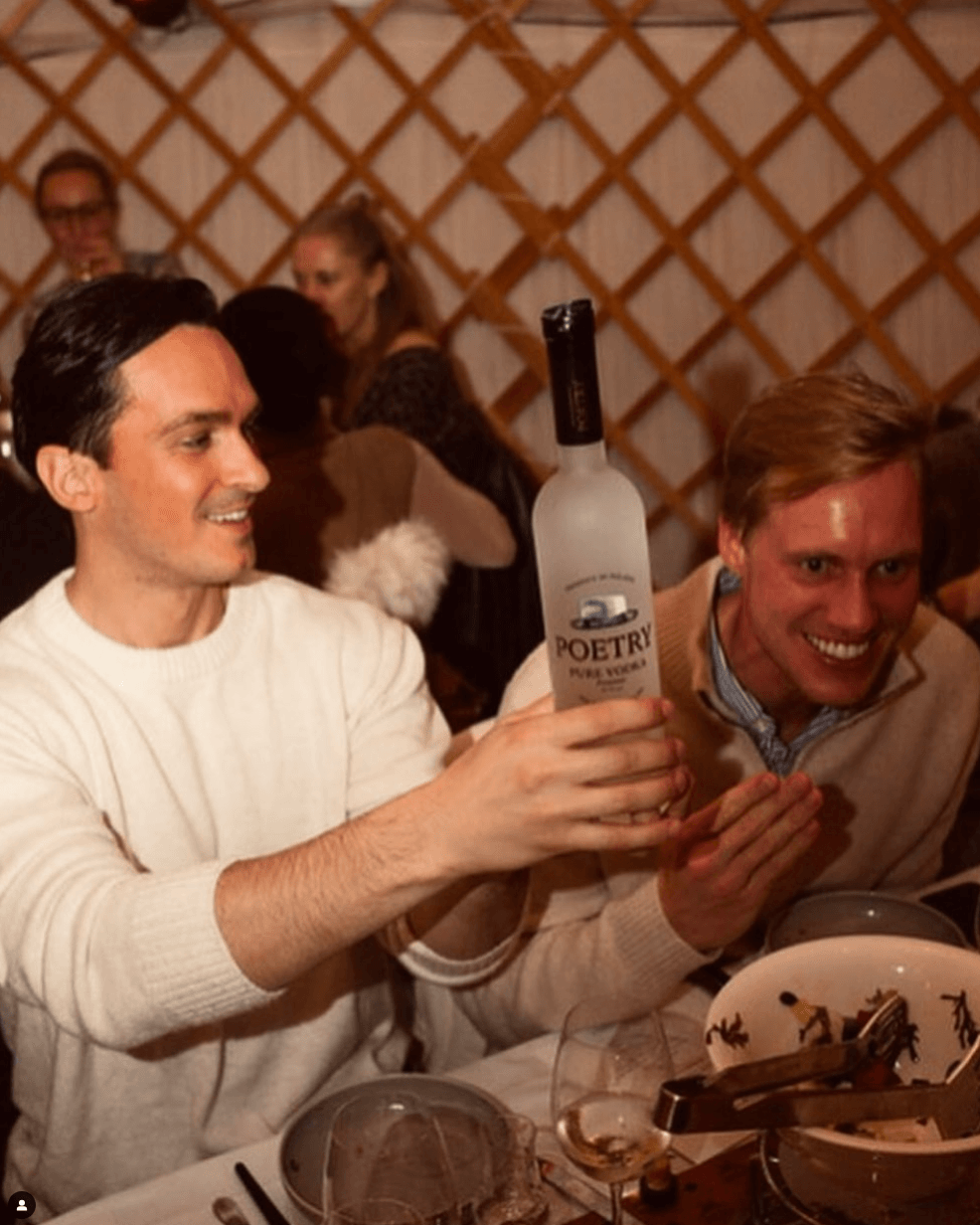 Zwei Freunde heben eine Flasche Poetry Vodka bei einer Party und genießen den Moment. Perfekt für den Genuss von Premium-Getränken wie Poetry Vodka von Dave Stewart, erhältlich bei PureBev.