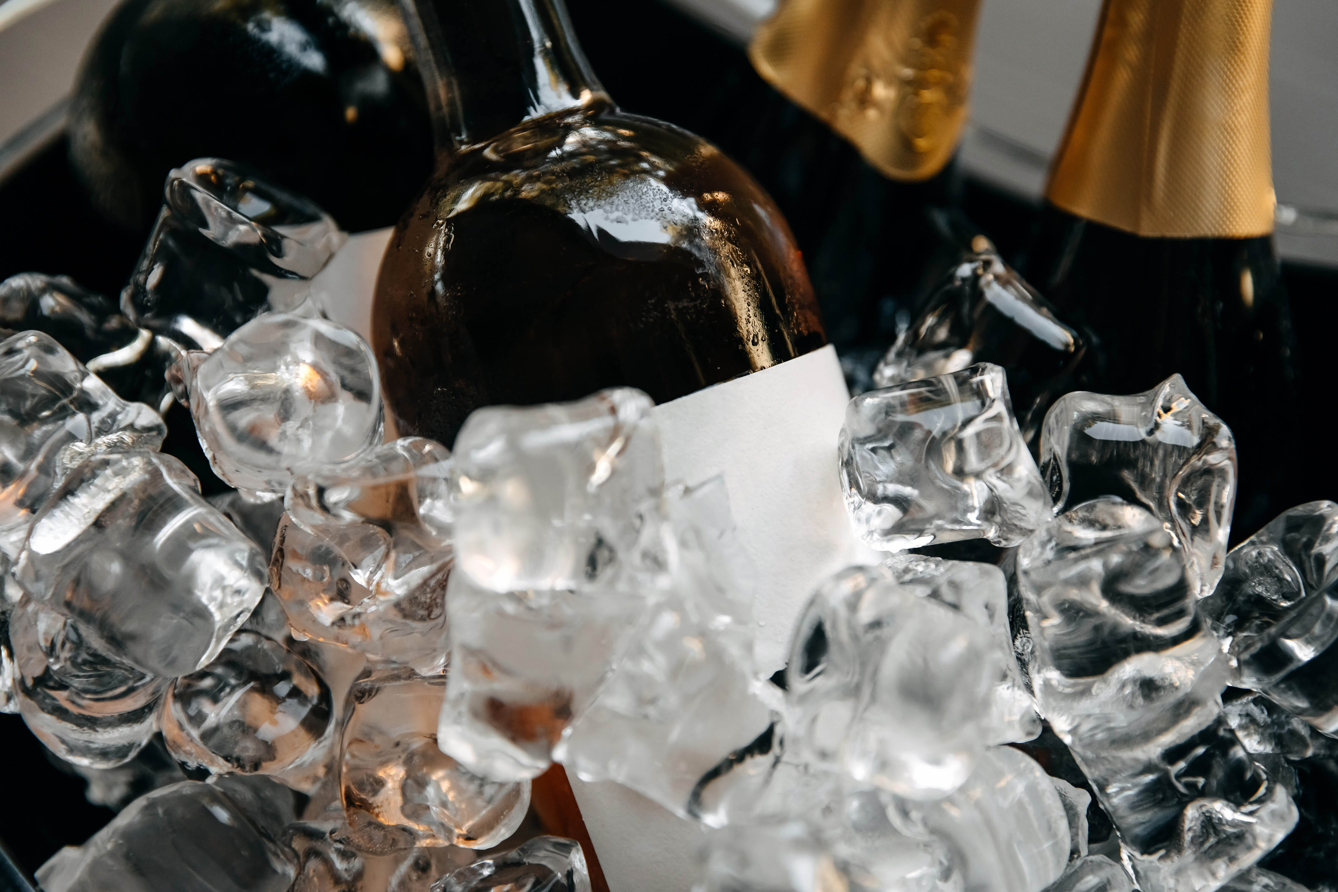 Nahaufnahme von Flaschen, die in einem Behälter mit Eis gekühlt werden. Die Flaschen haben teilweise goldene Verschlüsse und befinden sich inmitten klarer Eiswürfel. Getränke von PureBev in Eis gekühlt